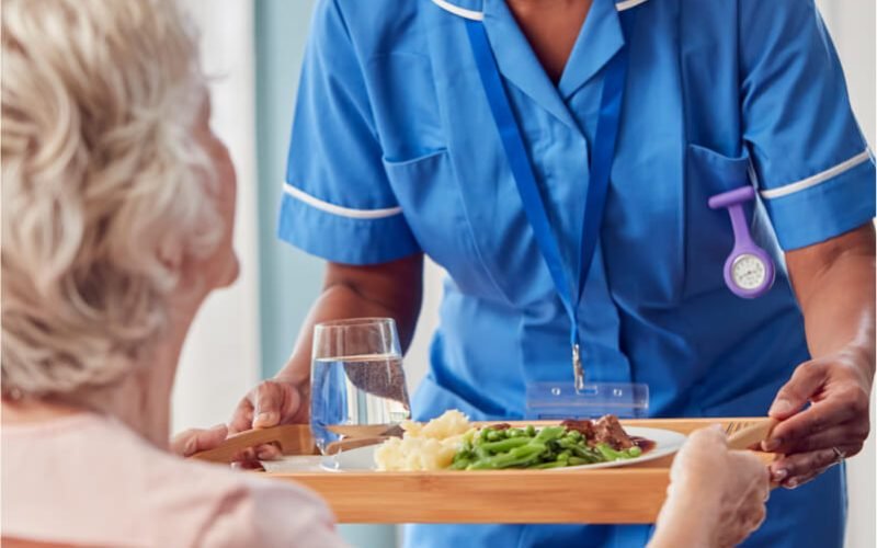 female-care-worker-in-uniform-bringing-meal-on-tra-2022-04-04-21-34-37-utc.jpg